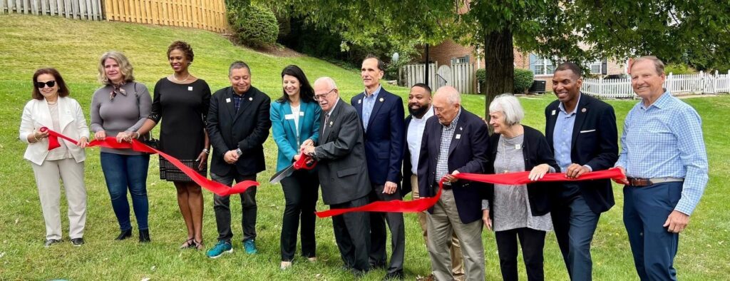 Ribbon cutting photo. Pictured from L to R: Former GSH Board Member Paula Lettice, GSH Board Member Laurie MacNamara, GSH Board Chair Erica McCants, Mason District Supervisor Andres Jimenez, GSH Executive Director Genee Hayes, Congressman Gerry Connolly, Mount Vernon District Supervisor Dan Storck, Delegate Rozia Henson, Former GSH Board Member Jim Sullivan, Joanna Sullivan, Franconia District Supervisor Rodney Lusk, GSH Board Member Pete Gartlan